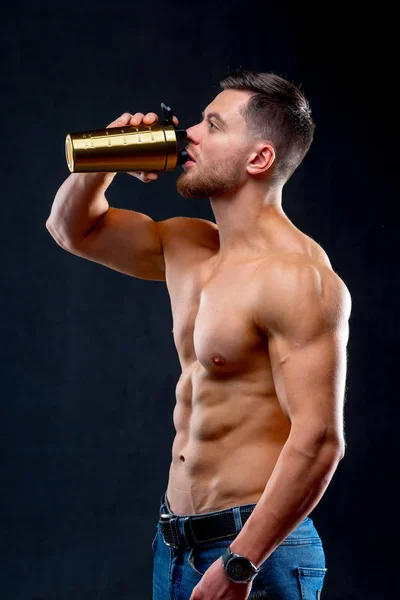 Студійний портрет красивого молодого культуриста, який тримає пляшку і пити, на чорному тлі. Напівголий спортсмен з сильним тілом . — стокове фото