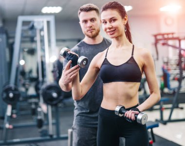 İçeride ağır halterlerle çalışan bir kadına kişisel antrenör yardım ediyor. Güzel bir kadın, spor salonunda egzersiz yapıyor..