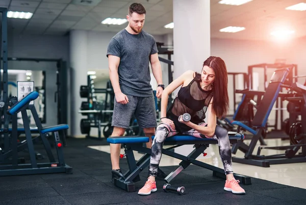 Sportliches Mädchen beim Krafttraining mit Unterstützung ihres Personal Trainers im Fitnessstudio. — Stockfoto