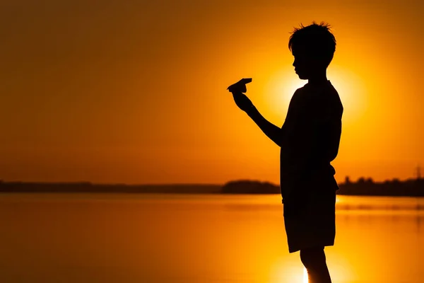 Ein glückliches Kind spielt bei Sonnenuntergang mit einem Papierflugzeug. Klassen mit Kindern im Freien. Lebensstil — Stockfoto