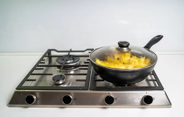 French Fries frying in a pan on a gas stove in white kitchen.