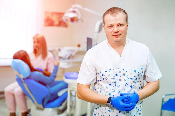 Médico invitando a la oficina del dentista y mirando a la cámara con la silla estomatológica y el paciente en el fondo . — Foto de Stock