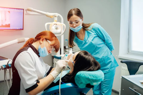 Zahnärztin und Krankenschwester in Masken und Schutzbrille, die die Zähne der Patienten behandelt. Stomatologe mit Assistentin in einer Zahnarztpraxis. Stomatologie und Gesundheitskonzept. — Stockfoto