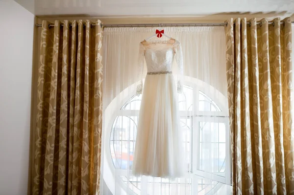 Amazing dress. Full length of beautiful silk wedding dress hanging near the window. Wedding day — 스톡 사진