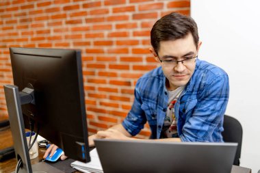 Genç adam ofisinde oturuyor ve masaüstü bilgisayarı üzerinde çalışıyor. İşadamı ofiste çalışırken bilgisayar monitörüne bakıyor.