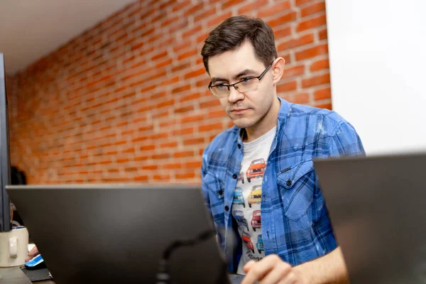 Seriös ung man koncentrerade sig på problem på PC-skärmen. Smart programmerare arbetar hårt inom IT-företaget inomhus. — Stockfoto