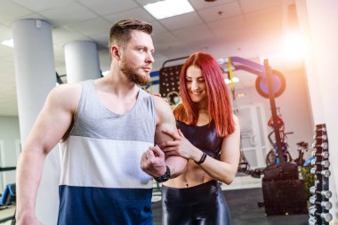 Fitness kulübündeki güzel kadınlara kaslarını gösteren güçlü bir atlet. Genç kadın, erkeğin kol kaslarına dokunuyor..