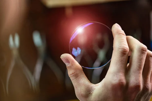 ophthalmologist hands showing a glass lens for spectacles. Blurred background. Ophtalmologist equipment. Vision correction concept. Closeup