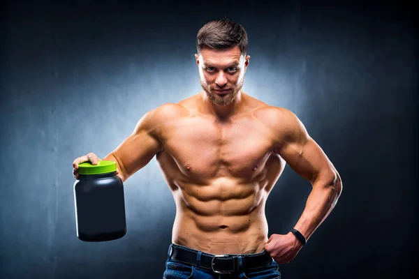 男子健美运动员 赤身裸体 手中拿着一罐运动营养品 在蓝色的背景下摆姿势 — 图库照片