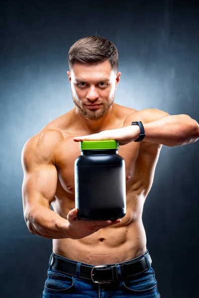 男运动员健美运动员手里拿着一罐运动营养品 在镜头前展示蓝色背景的姿势 — 图库照片