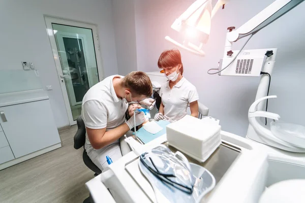 两名牙医检查女病人的牙齿以进行治疗 带显微镜的现代口腔科橱柜 口腔保健概念 — 图库照片