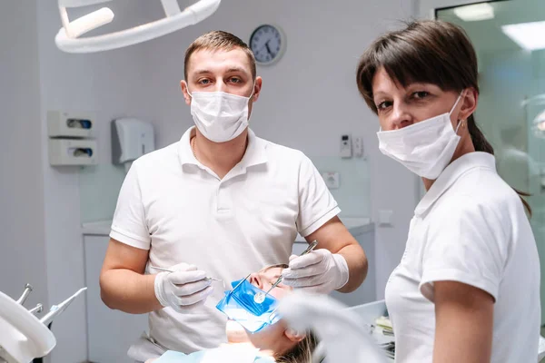 均一な歯科医は 現代のスタマトージーオフィスで患者に歯科治療を行います 選択的フォーカス 側面からの眺め — ストック写真