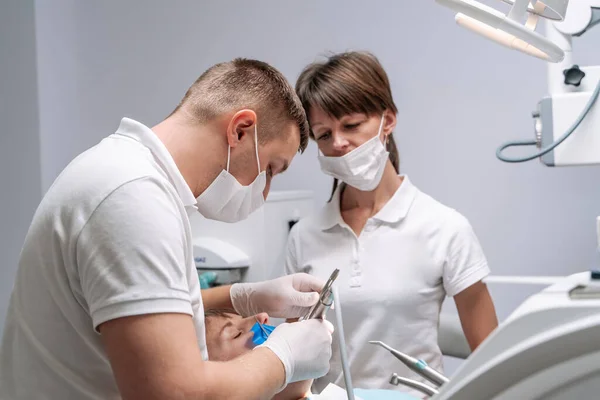 两名牙医对坐在椅子上的年轻女病人的牙齿进行口腔科治疗 口腔保健概念 — 图库照片