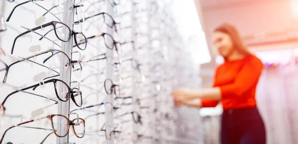 Óculos de prescrição para venda e em exposição em um escritório de óptica. Mulher em um fundo embaçado — Fotografia de Stock