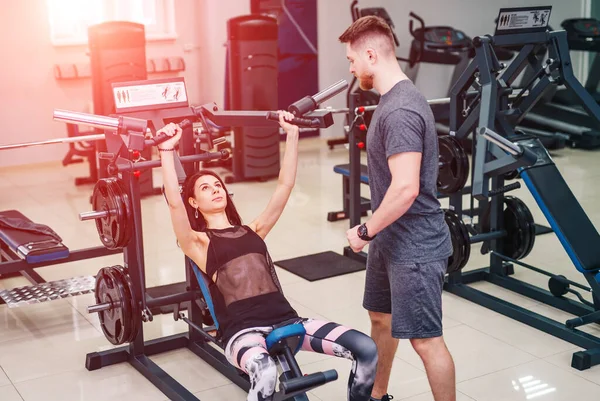 Personal Trainer hilft einer jungen Frau beim Heben einer Langhantel, während sie im Fitnessstudio trainiert. Selektiver Fokus. — Stockfoto