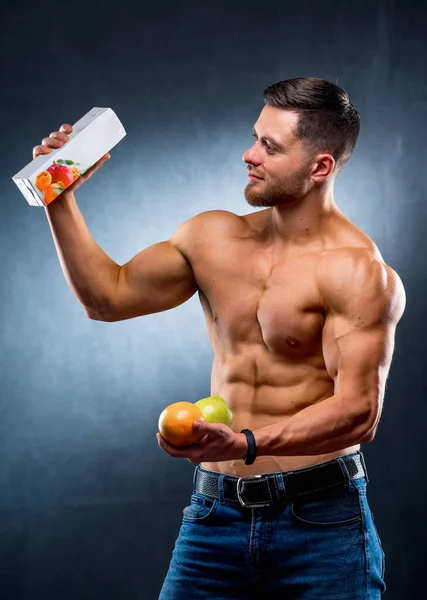 肌肉发达的运动员手里拿着果汁和水果 在新鲜食物和浓缩食物之间作出选择 赤身裸体 灰色背景 — 图库照片