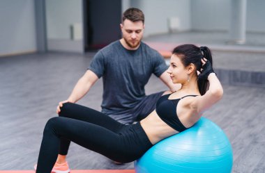 Antrenör, müşterinin spor salonunda egzersiz topuyla çalışmasına yardım ediyor. Spor ve yardım konsepti. Fitbol egzersizleri yapıyor.