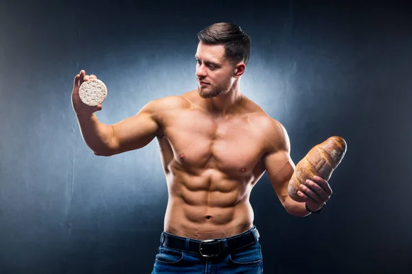 年轻的赤身裸体男子拿着麦片饼干和面包 在健康食物和有害食物之间作出选择 横向的照片 灰色背景 — 图库照片