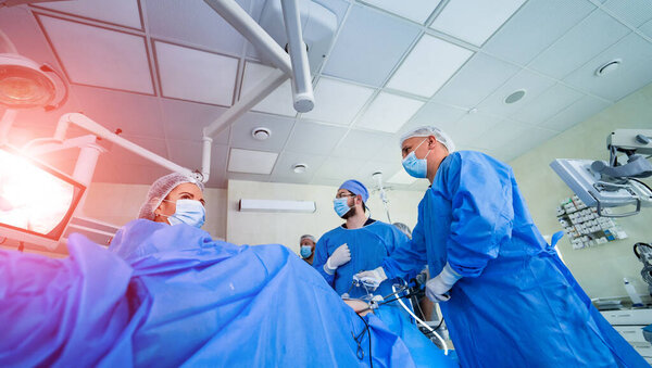 Группа врачей проводит операцию пациенту. Хирурги в медицинской форме и масках работают в операционной