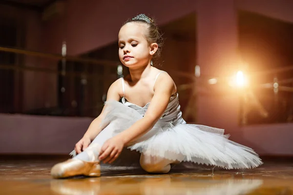 Premium Photo  Ballerina in a black body and white tights is sitting on  the wooden floor dancer touching her leg looking at camera on studio  background