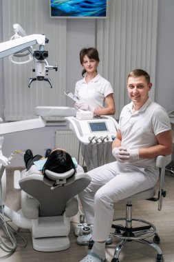 Diş hekimliği, ilaç, tıbbi ekipman ve stomatoloji konsepti. Diş hekimleri ve bir müşterisi olan modern diş sağlığı kliniğinin içi..