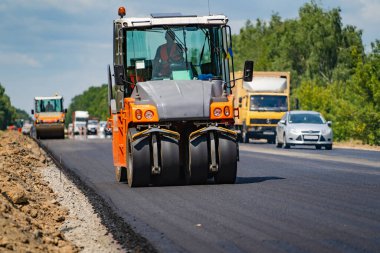Yol silindiri yeni asfaltı dümdüz ediyor. Ağır titreşim silindiri asfalt döşeyip yol tamiri yapıyor. Seçici odak.