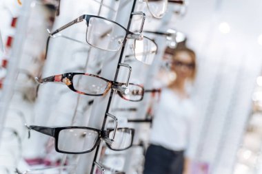 Optik dükkan. Optisyen gözlük öneriyor. Arka planda bir sürü gözlüklü kadın.