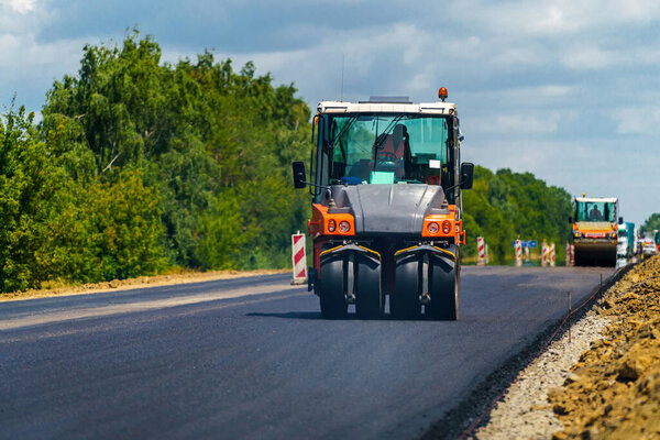 Road repair, compactor lays asphalt. Heavy special machines. Asphalt paver in operation. Side view. Closeup.