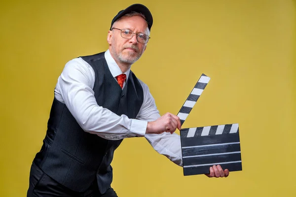 Senior smiling director with movie flap. Yellow background. Filming. Film directing. Film production. Human emotions.