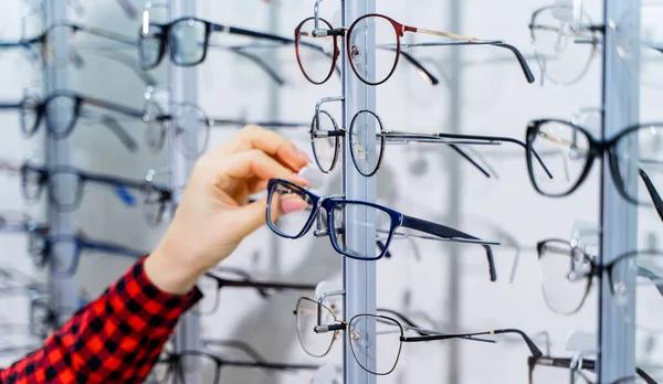 女性の手は眼鏡を選ぶ 眼鏡をかける 眼鏡の行は 光学で 眼鏡店 光学系の店に眼鏡をかけて立つ — ストック写真