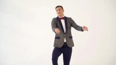 Kırmızı papyonlu gri takım elbiseli mizahçı, stüdyoda beyaz arka planda elinde kurdeleyle dans eden dansçı benzerliğinde dans ediyor.