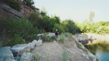 Gezgin bir sırt çantasının koşumları için el ele tutuşuyor ve taşların ve kayaların arka planında kıyıda yürüyor. Turist etrafındaki muhteşem manzaraya bakıyor.