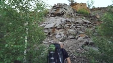Spor ekipmanlı turist bir kayaya tırmanıyor ve yükseklikten güzel bir yere bakıyor.
