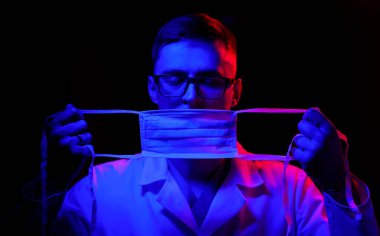 Coronavirus konsepti. COVID-19. Hasta muayenesinden önce yüz maskesi takan üniformalı genç bir erkek doktor. Doktorlar kahramandır. Koronavirüs salgını.