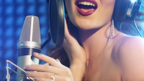 明るい口紅のきれいな女性がマイクを手に持ってオーディオスタジオでヘッドフォンで歌ってる — ストック動画