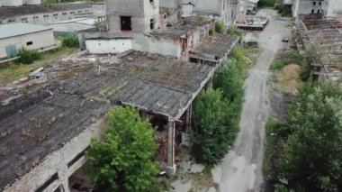 Hava görüntüsü. Eski bina harap oldu, çim ve çalılara kadar eğildi. Pencerelerinde kırık camlar olan terk edilmiş fabrika salonları. Yok edilen deponun olduğu kıyamet sahnesi.