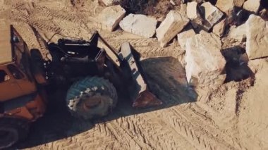 Özellikle teçhizatlı buldozer, taş ocağında ormanlı bir kayanın arka planında bir taş topluyor. Kum ocağının manzarası. Kamera hareketi yukarı.