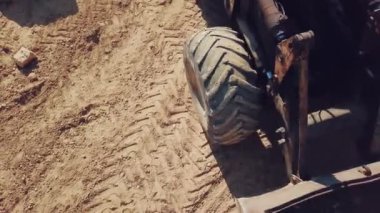 Kocaman tekerlekleri ve kovası olan buldozer kumlu bir taş ocağının bölgesinde hareket ediyor. Yakın plan.