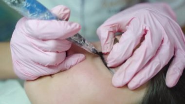 Kadınlar için kalıcı göz makyajı prosedürü. Usta müşterinin gözlerini profesyonel bir fırçayla iğneyle boyuyor..