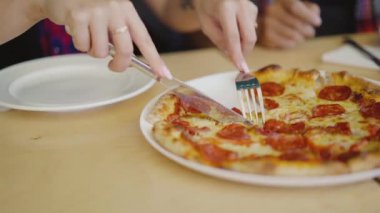 Kadın bir dilim sıcak pizza kesiyor ve pizzacının masasındaki tabağına koyuyor. Bulanık arkaplan