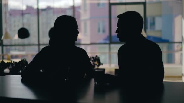 男と女のシルエットがカフェのテーブルで話してる窓の外で酒を飲んでる ぼやけた背景 — ストック動画