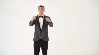 Papyonlu, kareli takım elbiseli bir adam stüdyoda beyaz bir arka planda maço tavırları sergiliyor..