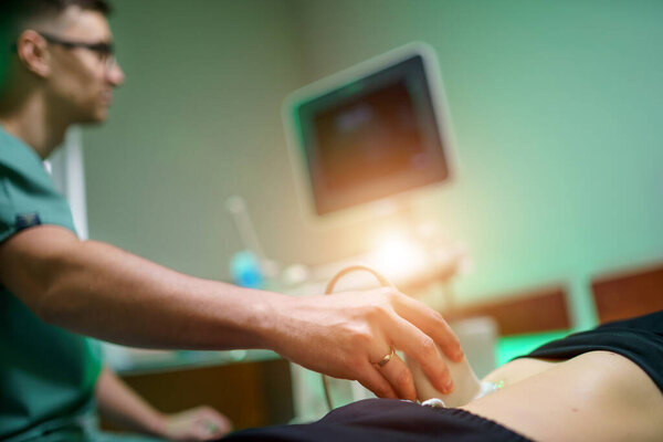 A young male doctor makes a patient an ultrasound of the abdominal cavity. Ultrasound scanner in the hands of a doctor.