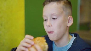 Restoranda hamburger yiyen aç bir çocuk. Fast food kafe. Zararlı besin