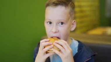 Şehirdeki kafede oturmuş patates kızartması ve hamburger yiyen genç bir çocuk. Fast food kafede bir çocuk. Zararlı besin