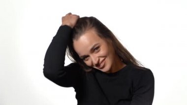 Siyah kazaklı muhteşem bir kız saçını arkaya atıyor ve stüdyoda beyaz bir arka planda gülümsüyor. Yakın plan.