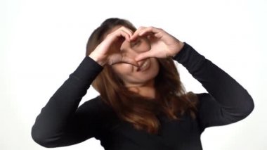 Stüdyoda beyaz bir arka planda güzel bir kadın kendi elleriyle kalbini gösteriyor. Sözsüz iletişim.