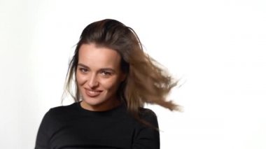 Uzun saçlı güzel bir kadın dönüp stüdyoda beyaz bir arka planda kameraya poz veriyor. Yakın plan.