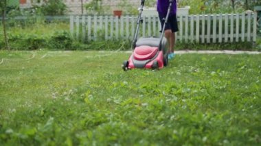 Bahçede çim biçme makinesiyle koşan bir çocuk. Bahçede çim biçiyorum. Yakın plan.