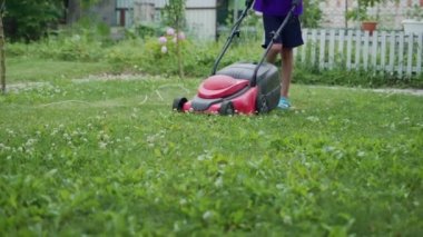 Genç bir çocuk yaz zamanı çim biçme makinesiyle çimleri kesiyor. Açık hava mevsimlik ev işleri